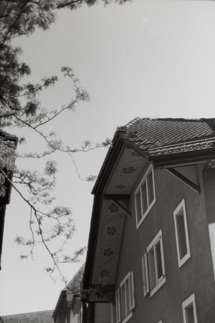 Schwarzweissfotografie von der Altstadt Aarau. Das Bild zeigt ein Haus mit bemalten Giebeln und ein paar Zweige eines Baumes.