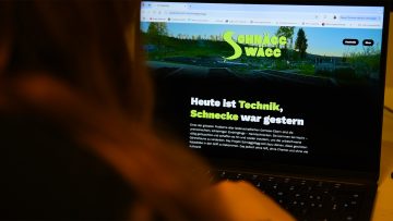 Website "SchnäggWägg" ist auf Laptop zu sehen, davor eine Frau, die auf dem Laptop scrollt.