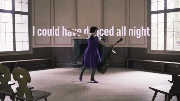 Eine Frau tanzt mit ihrem Cello in einem Pavillon und hinter ihr steht der Text "I could have danced all night"