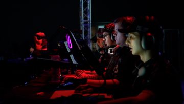 5 männliche Gamer welche im Dunkeln vor ihren Bildschirmen sitzen. Ihre Gesichter werden von den Bildschirmen erhellt.